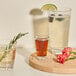 A Tossware Reserve Backbar highball glass filled with a brown liquid on a wooden board with other drinks and flowers.