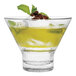 A Tossware Reserve Go-To Tritan plastic martini glass filled with green and yellow liquid, ice, and a brown object.