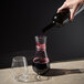 A hand pouring red wine from a Tossware plastic decanter into a glass.