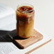 A Tossware plastic can glass filled with iced coffee on a wood board.