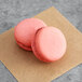 Two Coco Bakery raspberry macarons with pink filling on a brown paper.