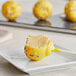 A Coco Bakery lemon cake pop with yellow cake and white icing and sprinkles on a white plate.