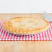 A Baker's Mark deep foil pie pan with a pie on a red and white checkered tablecloth.