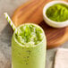 A glass of green smoothie with a straw and a bowl of green Dona Kyoto Ceremonial Matcha Powder.