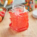 A 16 oz. clear square PET jar filled with red candy on a table.