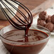 A whisk being stirred in a bowl of TCHO dark chocolate.