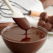 A bowl of TCHO Hella Dark chocolate with a spoon stirring it.