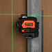 A Klein Tools black and orange laser level on a metal pole with a green laser beam.