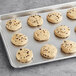 Preformed Otis Spunkmeyer chocolate chip cookie with chocolate chips on a baking sheet.