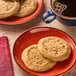 Two Otis Spunkmeyer peanut butter cookies on a red plate with a cup of coffee.