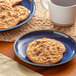 A plate of Otis Spunkmeyer Oatmeal Raisin cookies and a mug of coffee on a table.