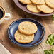 A blue plate of Otis Spunkmeyer sugar cookies on a table with a cup of coffee.