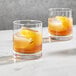 Two Della Luce rocks glasses filled with ice and whiskey with orange slices.