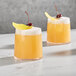 Two Della Luce Dion rocks glasses filled with orange juice with lemon and cherry garnishes.
