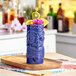 An Acopa blue ceramic tiki mug filled with fruit on a wooden tray.