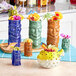 A group of colorful tiki mugs filled with fruit on a counter.
