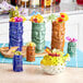 A group of colorful Acopa blue ceramic tiki shot glasses with fruit in them.