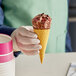 A hand in a white glove holding a Wicked Kitchen Vegan chocolate and red berry ice cream cone.