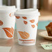 Two EcoChoice paper hot cups with orange leaf print on a table.