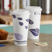 Two EcoChoice leaf print paper hot cups with a PLA lid on a table with coffee and a muffin.