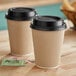 Two brown Choice paper coffee cups with black lids on a table.