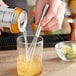 A stainless steel square tip mini whisk in a glass container with yellow liquid.
