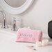 A pink Monarch Brands coral fleece washcloth next to a mirror with a black makeup bag.