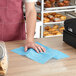 A person cleaning a bakery counter with a blue Tork food service wiper.