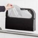 A hand pulling a Tork Universal half fold toilet seat cover from a white dispenser.