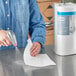 A woman using a spray gun to clean a professional kitchen counter with a Tork paper towel.