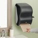 A hand using a black Tork automatic paper towel dispenser to get a hand towel.