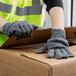 A person wearing Cordova Economy weight gray polyester/cotton work gloves opening a box.