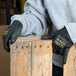 A person wearing Cordova Monarch black engineered fiber cut-resistant gloves with black polyurethane palm coating holding a piece of wood.