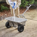 A person pouring white powder from a Chapin stainless steel spreader into a wheelbarrow.