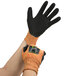 A pair of hands wearing orange and black Cordova heavy duty work gloves.