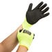 A pair of green Cordova Monarch gloves with black foam latex palm coating and yellow trim on a person's hands.