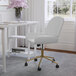 A Martha Stewart white faux leather swivel office chair with a gold base in front of a window.