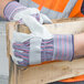 A person wearing Cordova striped canvas work gloves holding a piece of wood.
