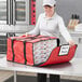 A woman holding a red Choice insulated pizza delivery bag with pizza boxes inside.