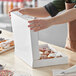 A white rectangular bakery box being opened, containing assorted donuts.