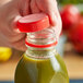 A hand using a red unlined tamper-evident cap to close a bottle of green liquid.