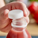 A hand holding a plastic bottle of red juice with a white tamper-evident cap.