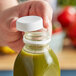 A hand using a white tamper-evident cap to open a bottle of green juice.