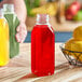 A person holding a 16 oz. Square Milkman PET clear juice bottle full of red liquid next to a bowl of yellow lemons.
