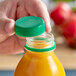A hand using a dark green tamper-evident cap to open a plastic juice bottle.