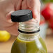 A hand holding a Black Unlined Tamper-Evident Cap over a bottle of green juice.
