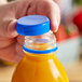 A hand holding a plastic bottle of juice with a royal blue cap.