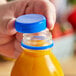 A hand opening a plastic bottle of juice with a Royal Blue plastic cap.