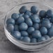 A glass bowl of Albanese milk chocolate covered dried blueberries on a table.