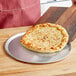 A cheese pizza on a DoughMakers aluminum pizza pan on a wooden surface.